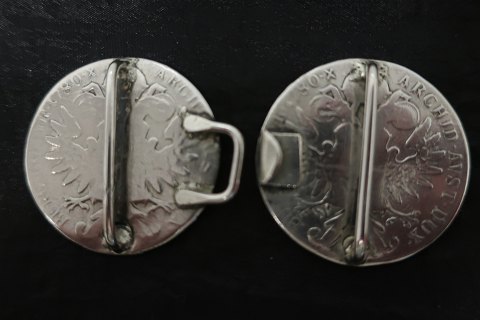 Bæltespænde af sølv
Lavet af 2 østriske mønter
Forsiden med tekst:
R-IMP-HU-BO-REG-M.THERESIA
(Mother Theresia af Habsburg)
Nederst står: S.F.
Bagsiden: 
Med ørn og indskrift: BURG-CO-TYR-1780-X-ARCHID-AVST-DUX
Også med inskriptioner på kant