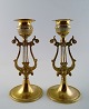 A pair of lyre-shaped brass candlesticks.

