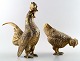 2 brass table decorations in the shape of a rooster and a hen.
