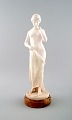 Stor figur af nøgen kvinde i alabast på marmor sokkel.
