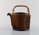 Gutte Eriksen: f. Rødby 1918, d.
Unique teapot of stoneware with handle in wicker.