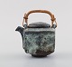 Gutte Eriksen, own workshop. Miniature teapot in glazed stoneware with handle in 
bamboo. Raku-burnt technique. 1950