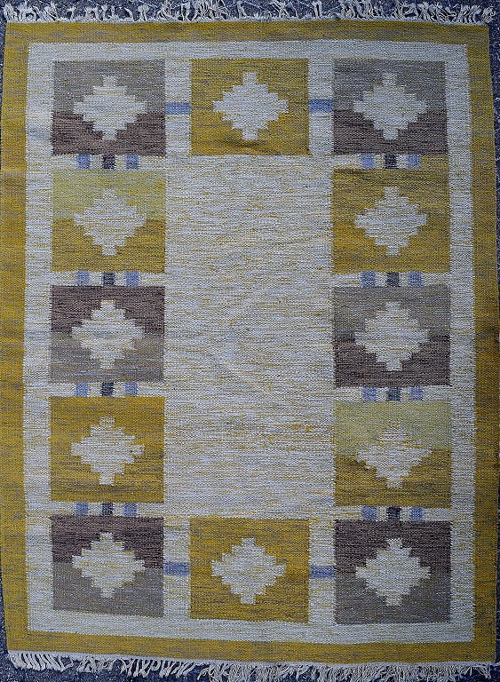 Rölakan tæppe med geometrisk mønster i gule og brune nuancer. 
