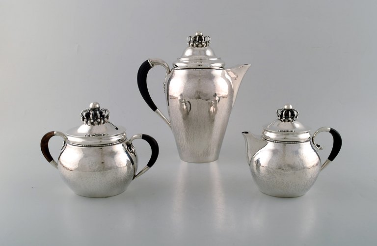 Rare Georg Jensen coffee service in sterling silver with ebony handles. Coffee 
pot, sugar bowl and cream pot. Lid shaped as royal crown. Dated 1915-30.
