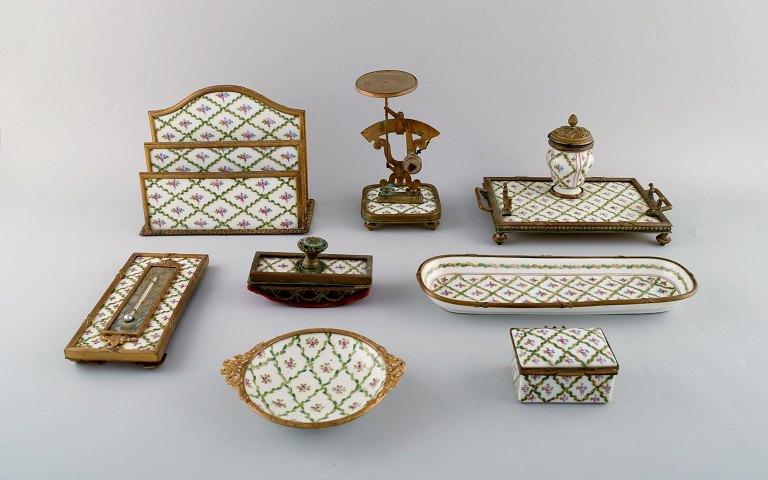 Sevres / Limoges style. Desk garniture in hand-painted porcelain and brass. 
Early 20th century. Paper weight, letter holder, ink well, ink cleaner, pen 
tray, etc.
